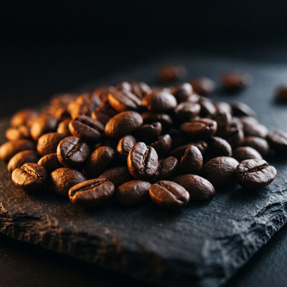 Freshly roasted medium roast coffee beans heaped on dark slate, oils catching warm light